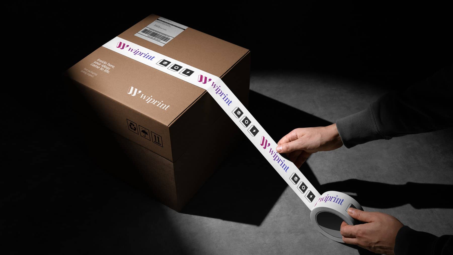 Hands pulling branded WiPrint packing tape across a sealed kraft shipping box.