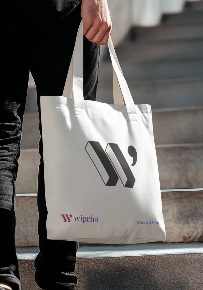 A person carrying a natural cotton tote bag printed with the WiPrint logo down a stairway.
