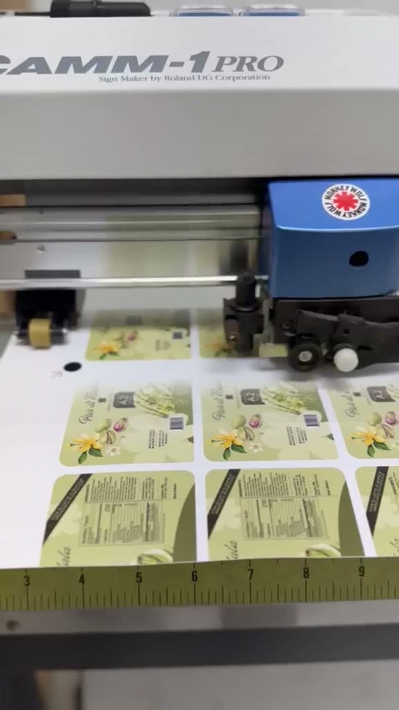 A plotter blade tracing the outline of a floral label mid-sheet