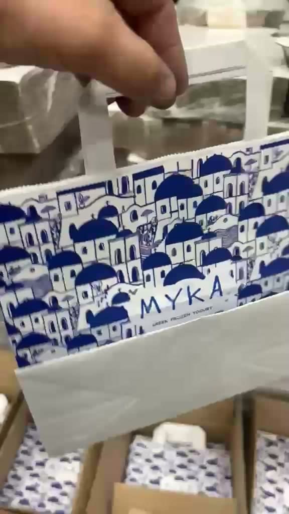 A MYKA paper bag printed with a blue Santorini rooftop pattern