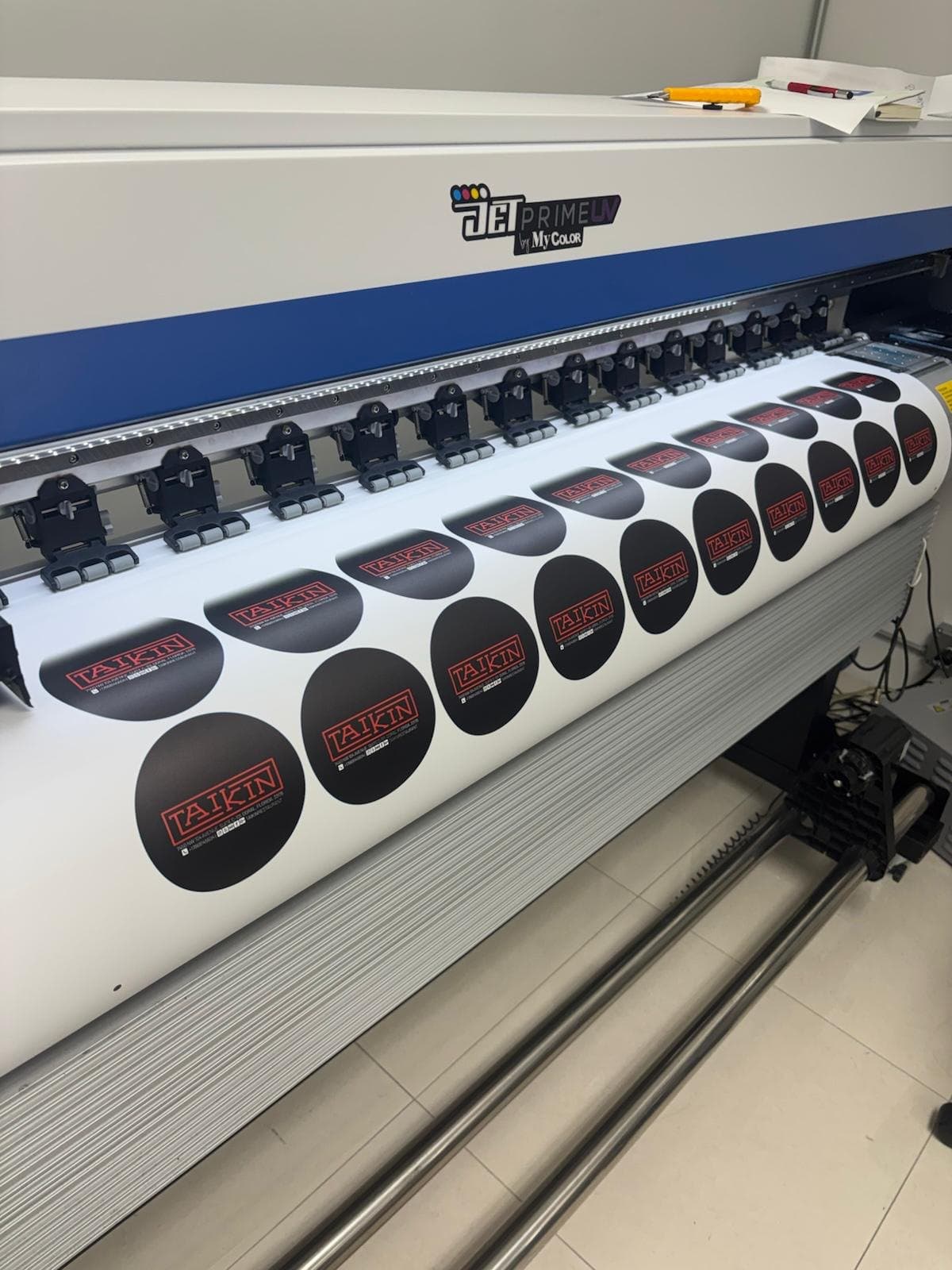 Round black labels printing on the UV press, a row of print heads above the roll